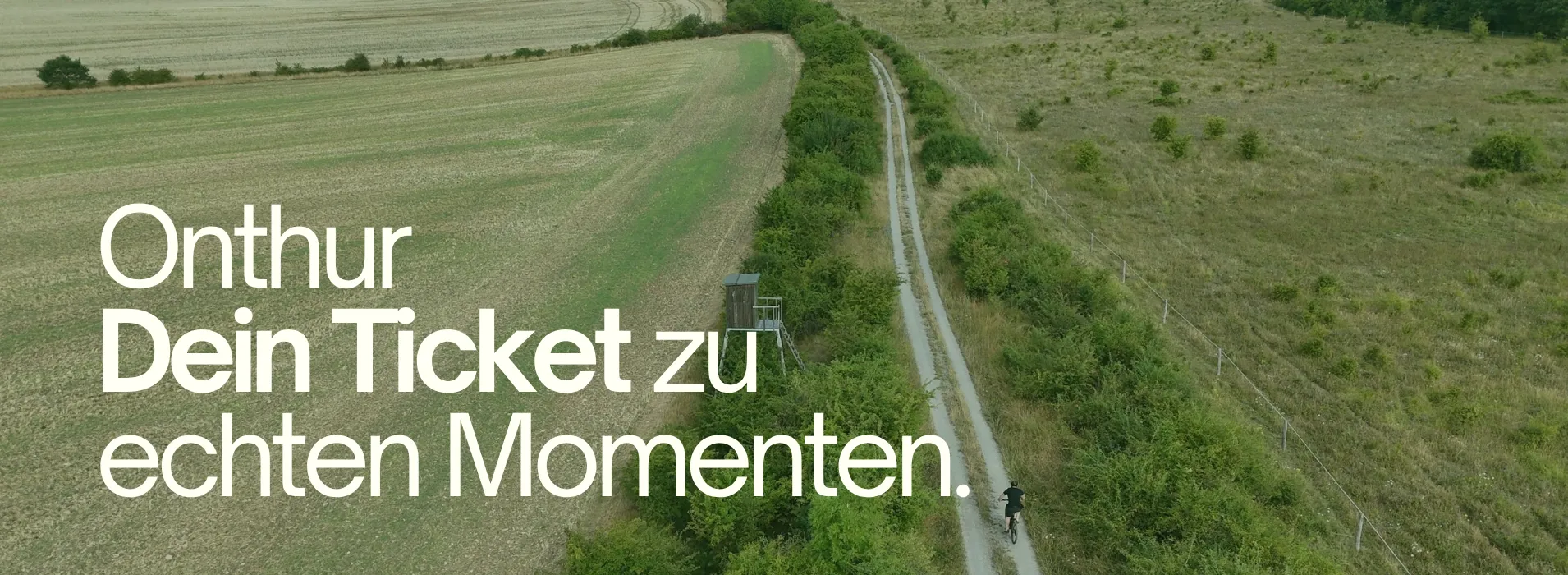 Luftaufnahme eines Radfahrers auf einem schmalen Feldweg neben einer kleinen hölzernen Beobachtungsplattform; links der Text ‚Onthur – Dein Ticket zu echten Momenten‘